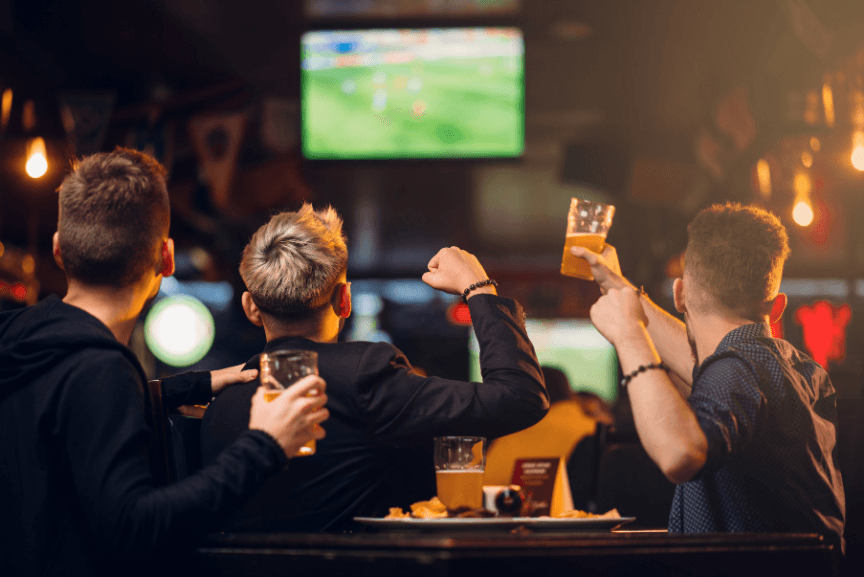 Publikum som ser fotball på storskjerm på en pub, med ølglass i hendene