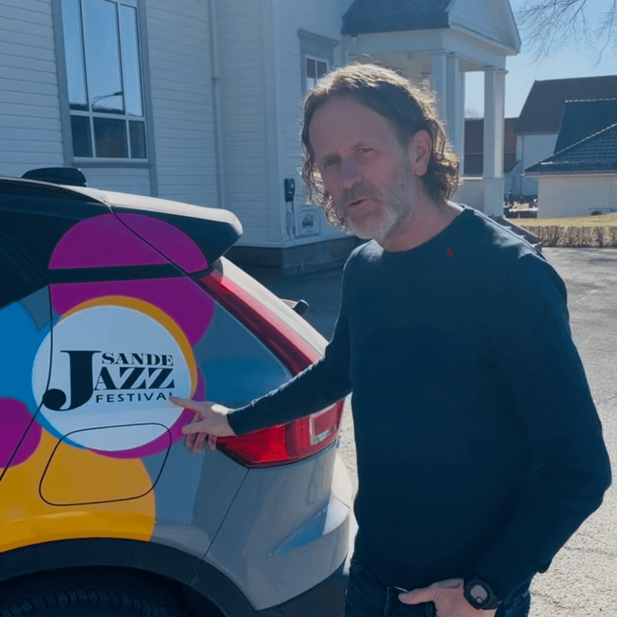 En mann ved siden av en bil dekorert med Sande Jazzfestivals logo